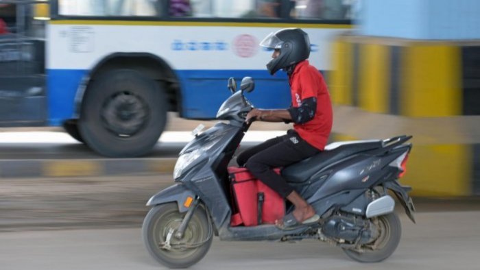 Delivery person driving a scooter carrying a delivery bag